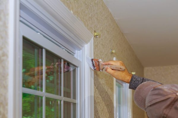 Hand with paintbrush painting a window frame trim white