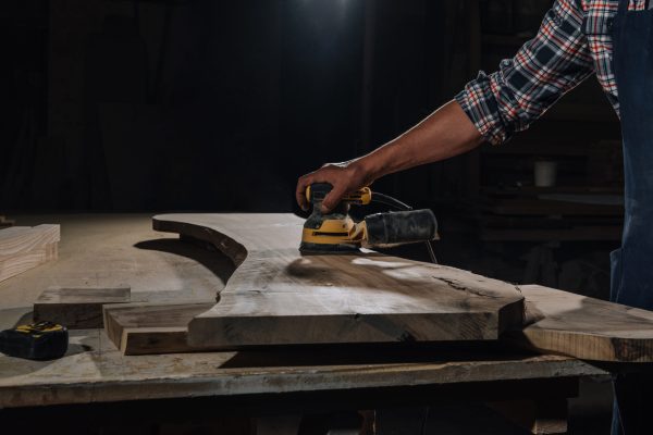 partial view of carpenter working with electric plane at workshop