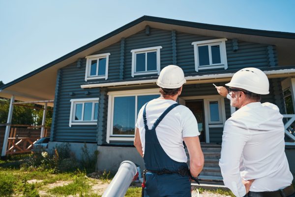 Housebuilders looking at front of the house while pointing at it with pencil and discussing next steps